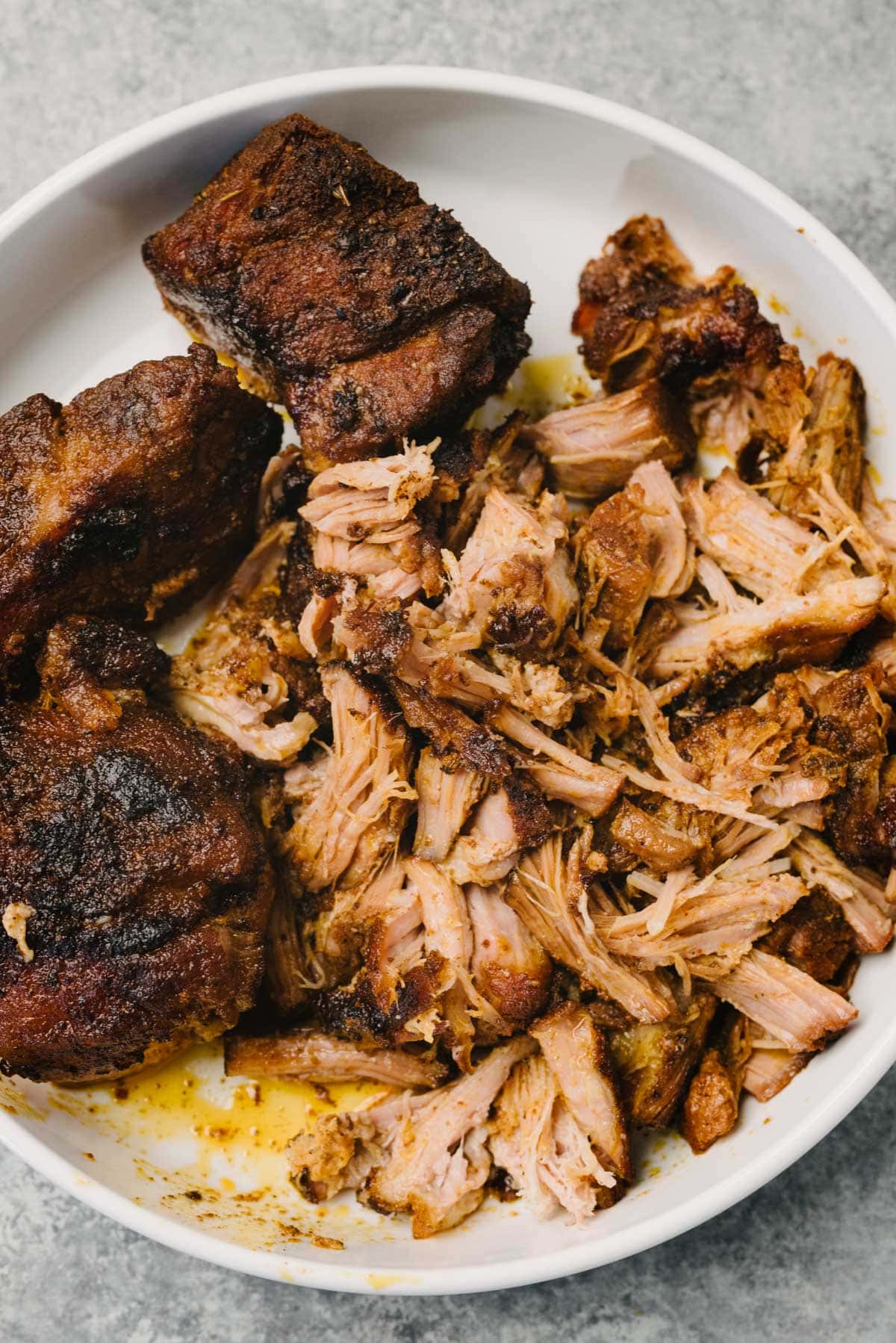 Partially shredded pulled pork in a large shallow white bowl.