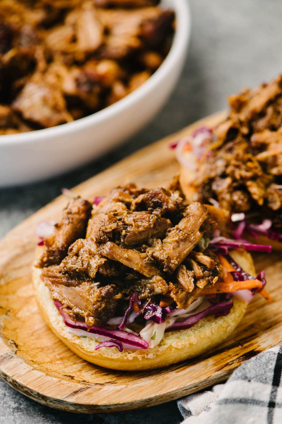 Side view, two open faced pulled pork sandwiches on a wood cutting board; a serving bowl of shredded Instant Pot pulled pork is in the background.