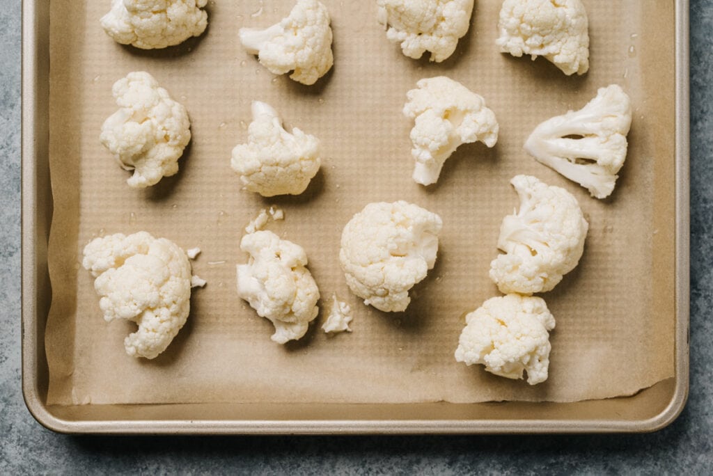 Cauliflower florets tossed with olive oil, salt, and pepper arranged in a single, even layer on a parchment lined baking sheet.
