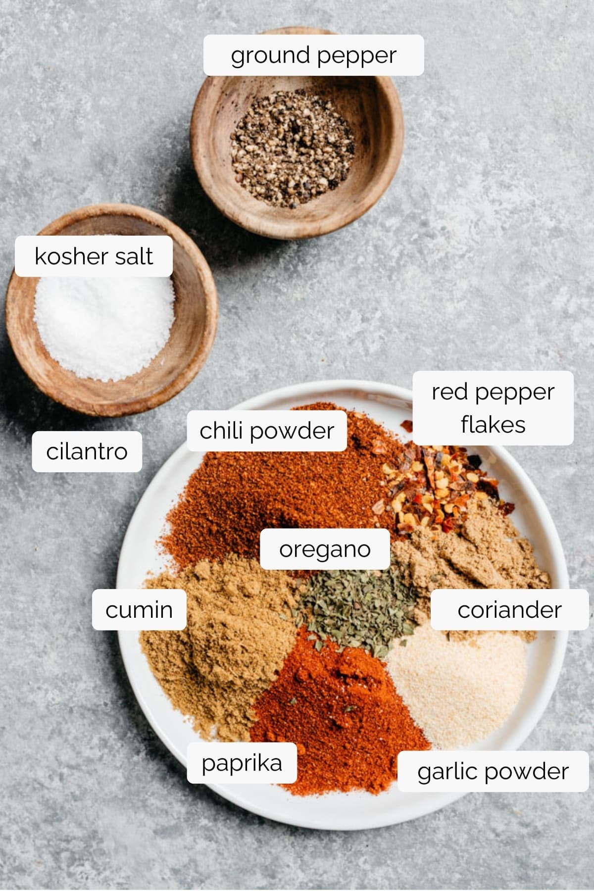 The spices for homemade taco seasoning arranged on a white plate and in small bowls on a concrete background.
