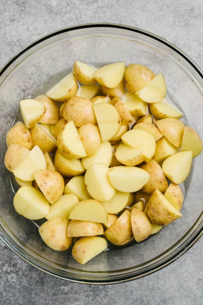 Diced baby gold potatoes in a glass mixing bowl with water and salt.