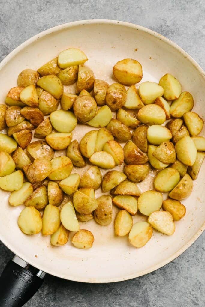 Crispy pan fried potatoes in a white skillet.